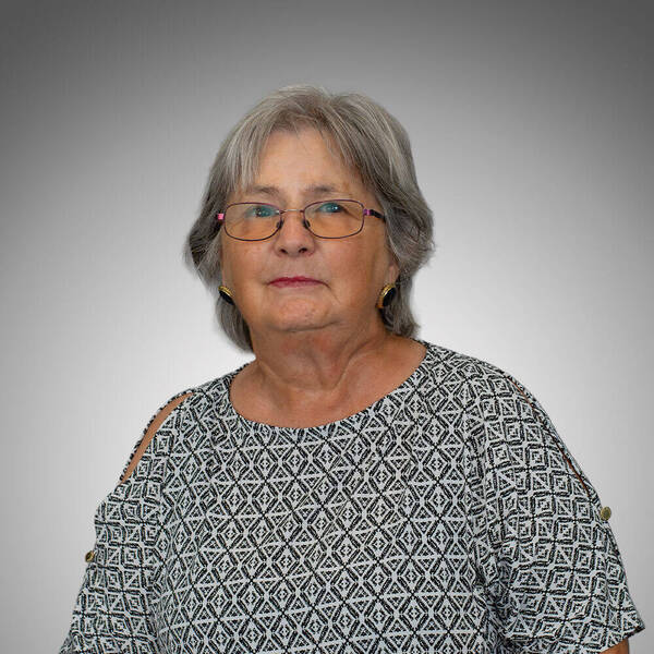 Woman smiling softly with gray hair, pink glasses, and a black and white geometric patterned cold-shoulder top.